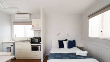 A compact hotel room with a kitchenette, a bed with blue and white bedding, and a window with curtains.