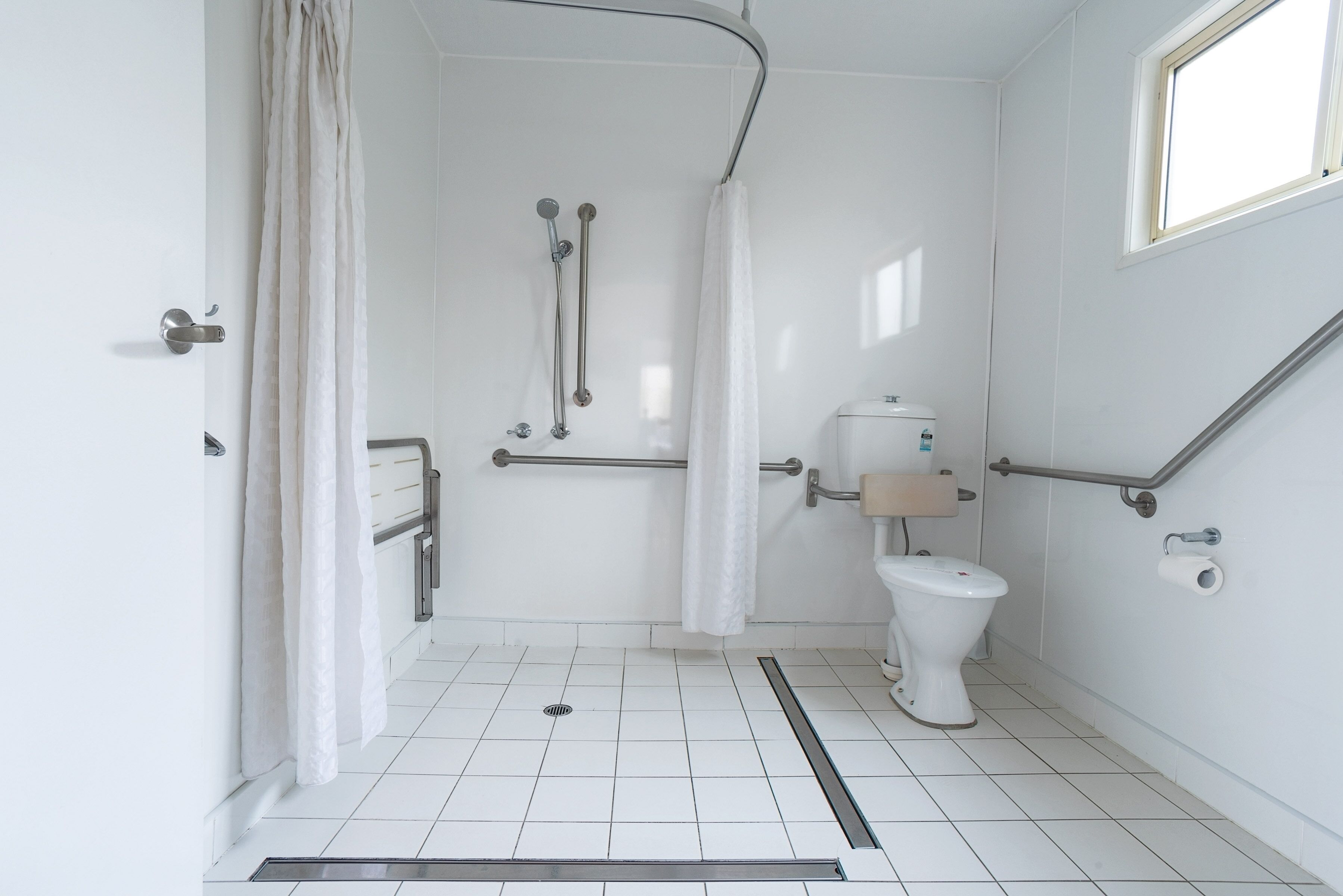 A modern bathroom with a walk-in shower, grab bars, a toilet, and a window.