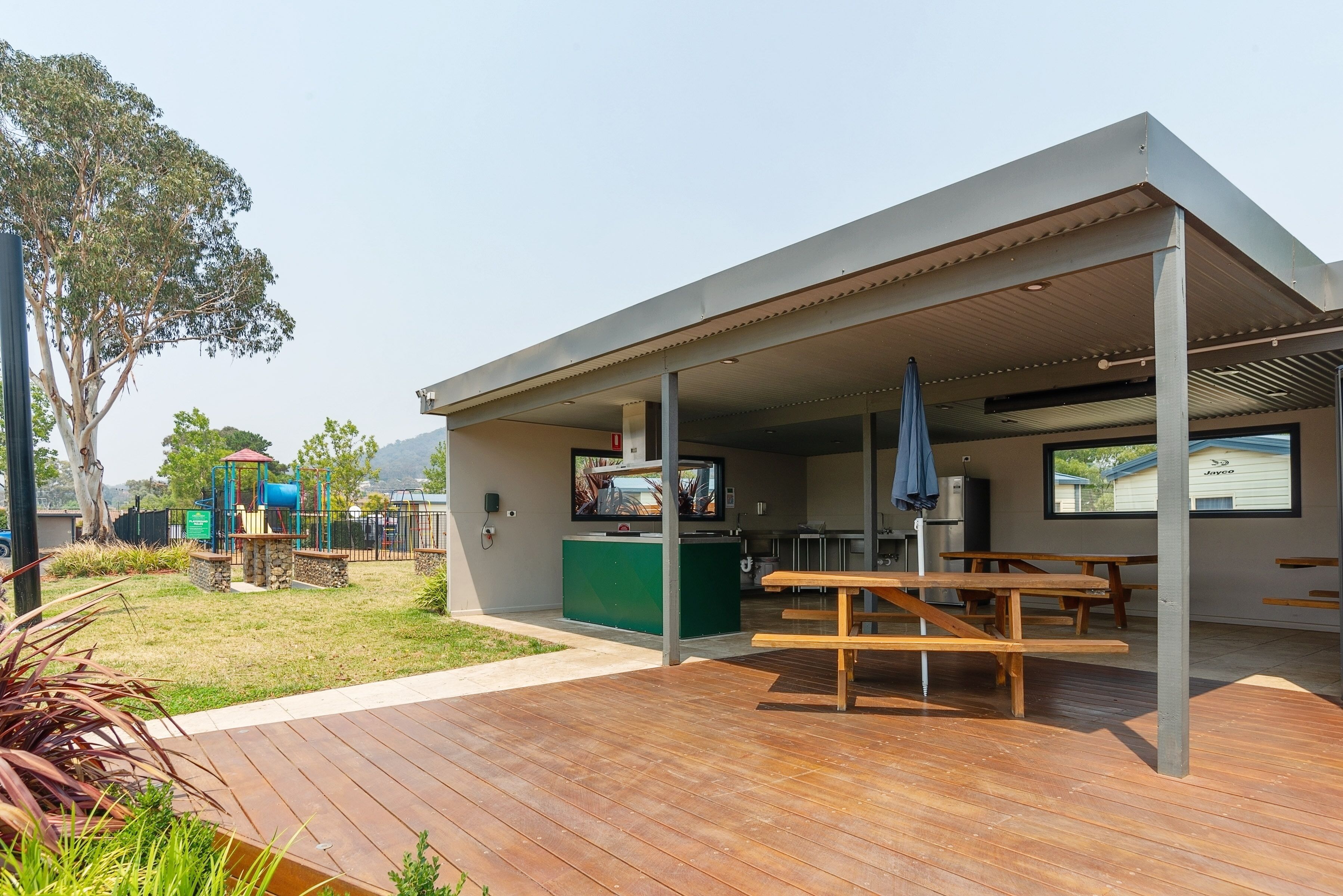 A covered outdoor area with picnic tables, a play structure, and a television screen.