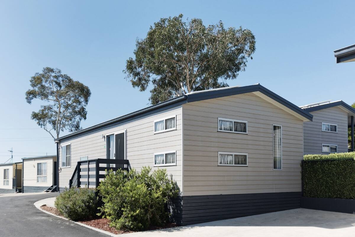 A modern mobile home with a flat roof, multiple windows, and a small front porch.