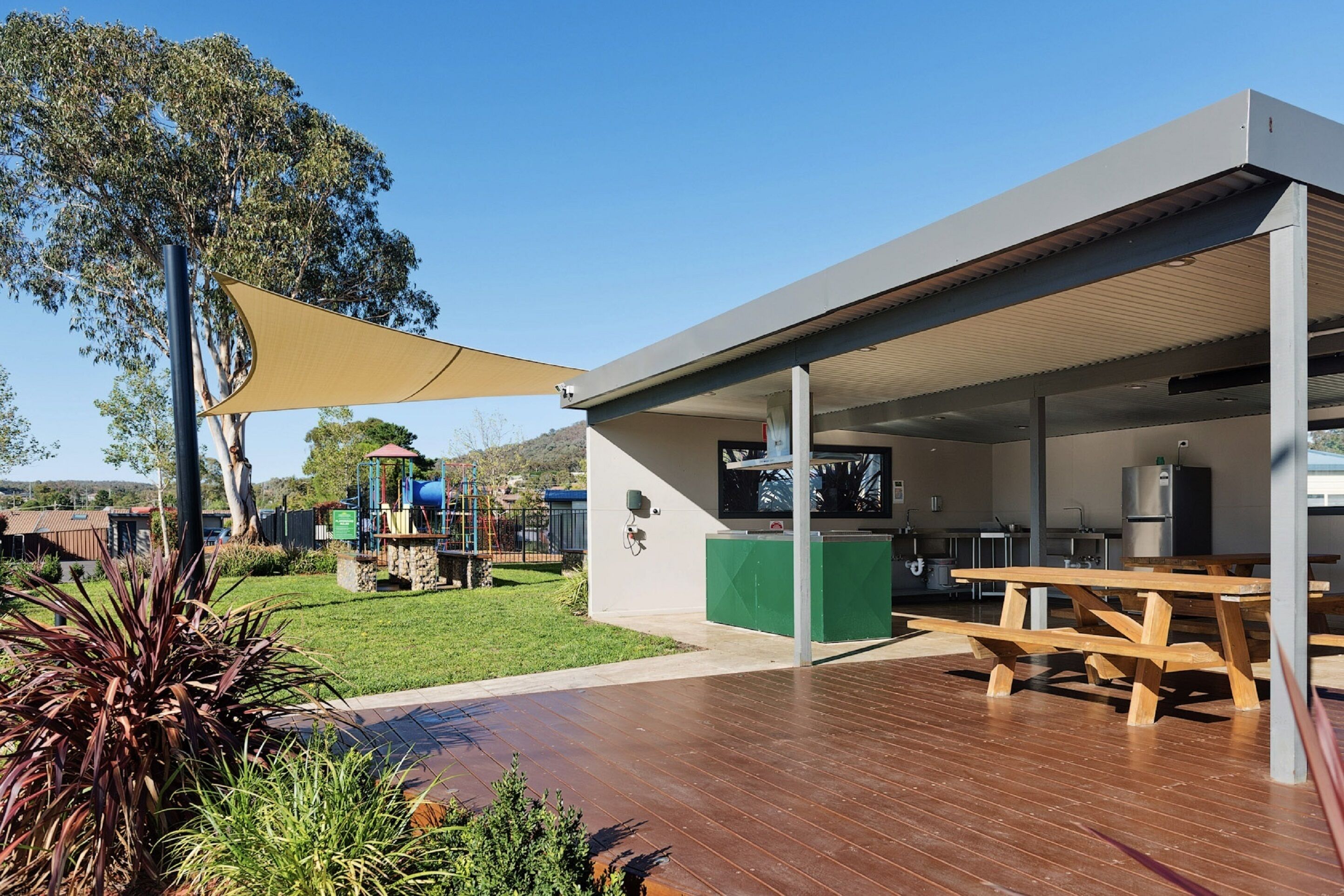 A modern outdoor patio area with a wooden deck, picnic tables, and a shaded area.