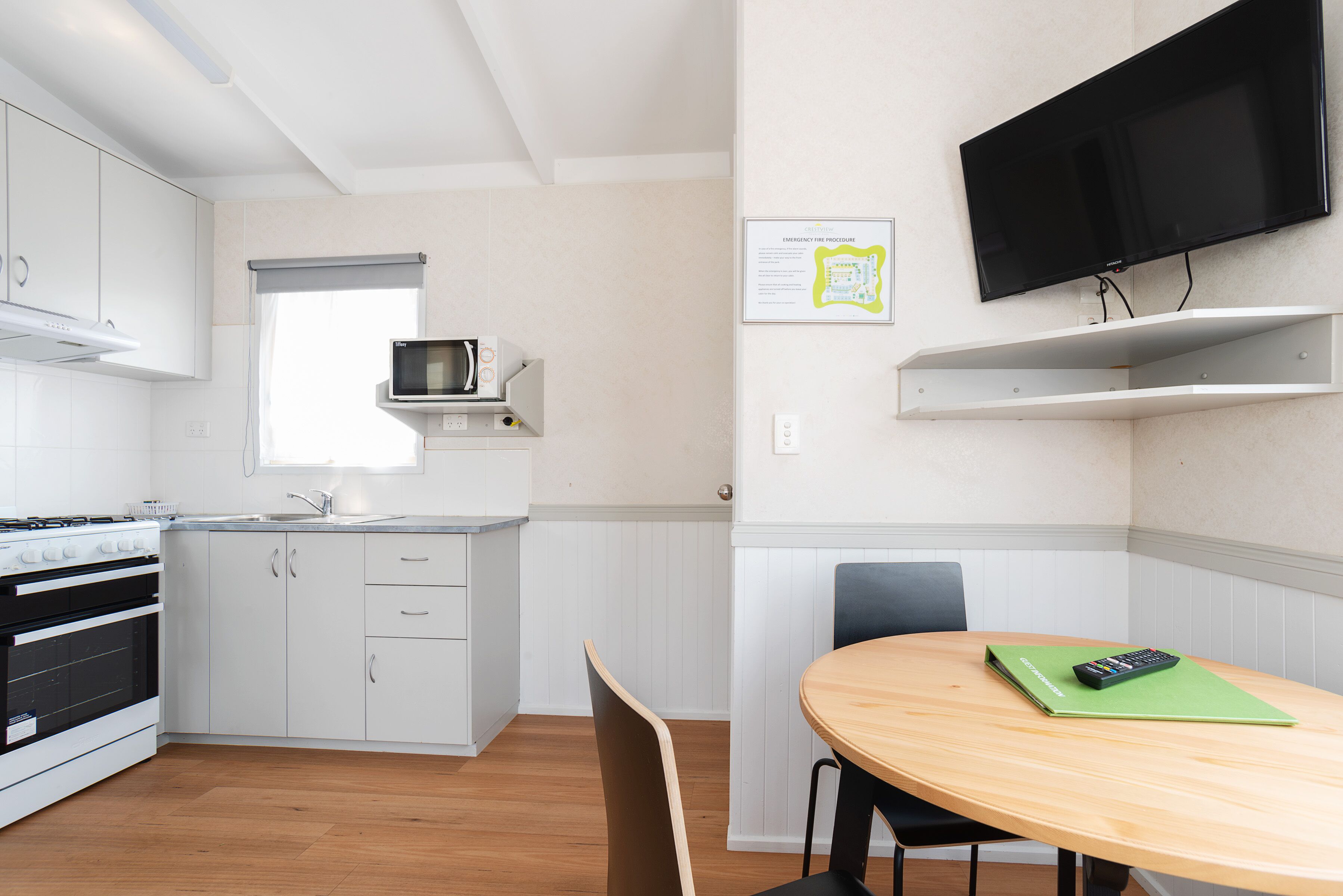 Una cucina moderna con mobili bianchi, forno a microonde integrato e un tavolo da pranzo in legno con una cartella verde e un telecomando.