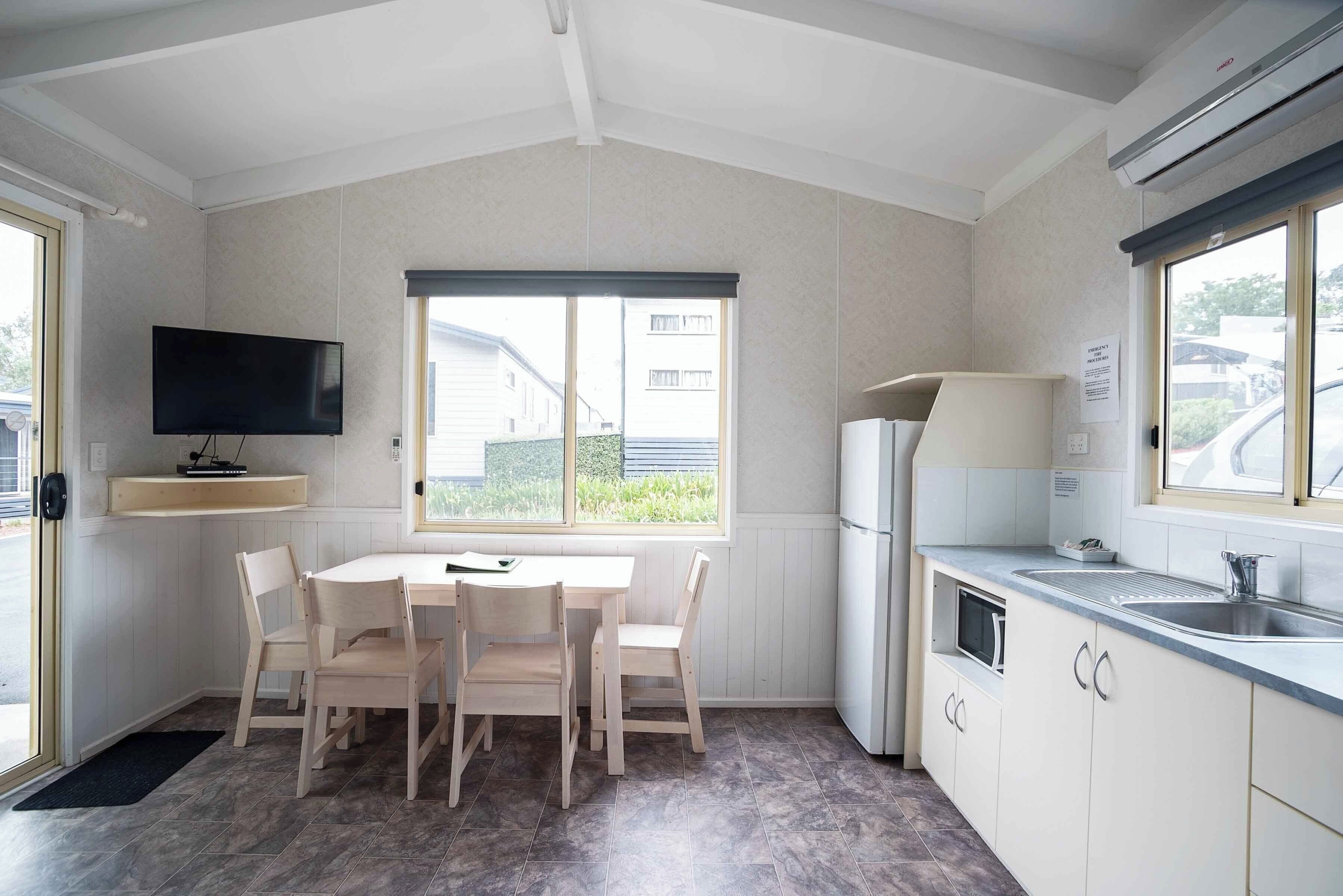 A modern kitchen with a dining area, a flat-screen TV, and a large window.