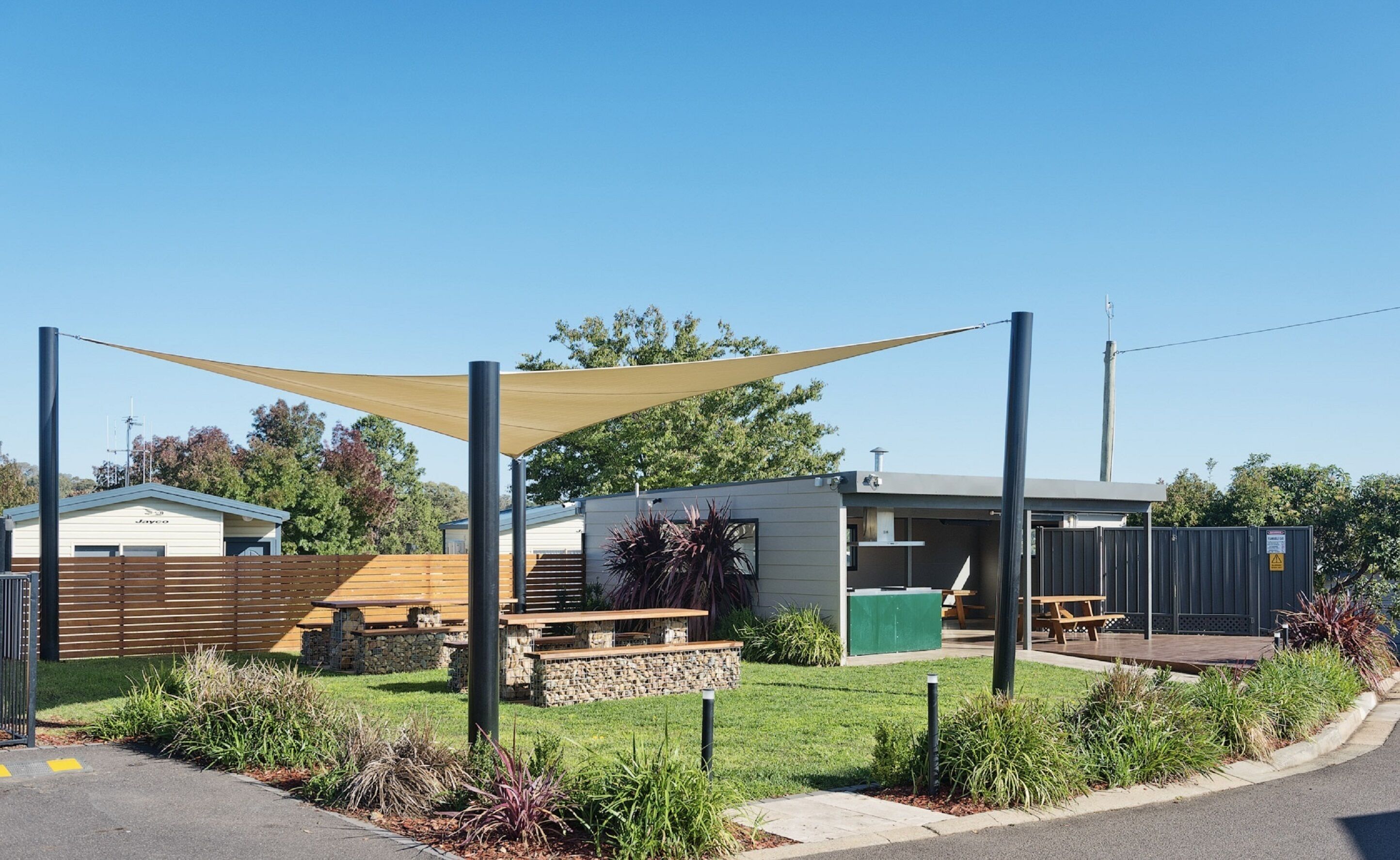 Un espace extérieur moderne doté d’une terrasse en bois, de sièges en pierre et d’un espace ombragé avec un auvent.