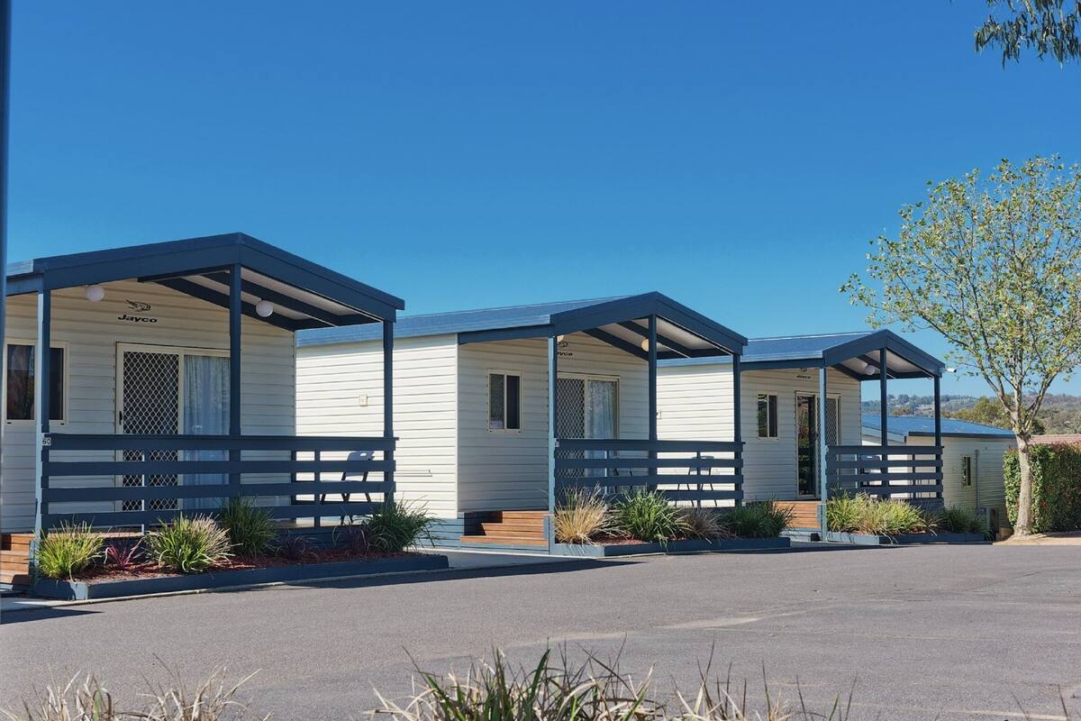 A row of mobile homes with a covered porch and a small garden area in front.