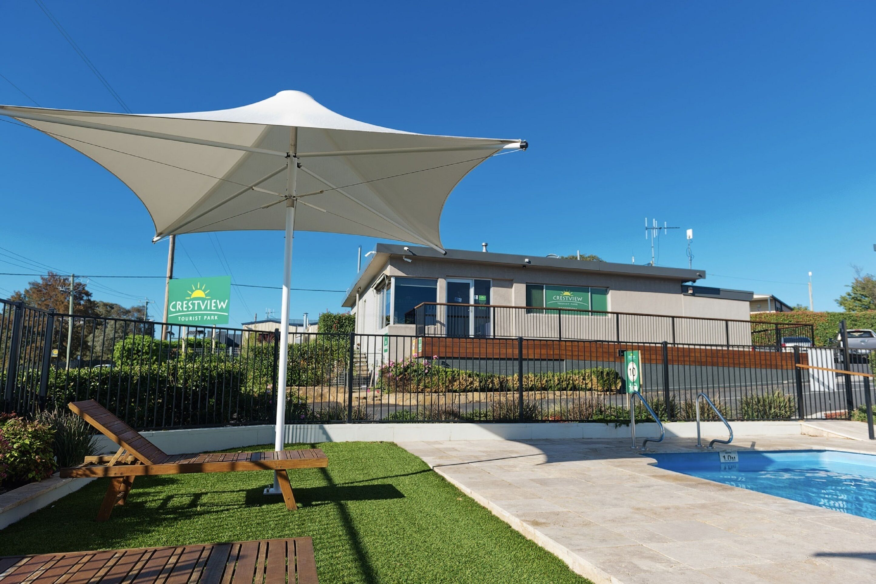 A pool area with a lounge chair, a large umbrella, and a sign for Crestview Tourist Park.