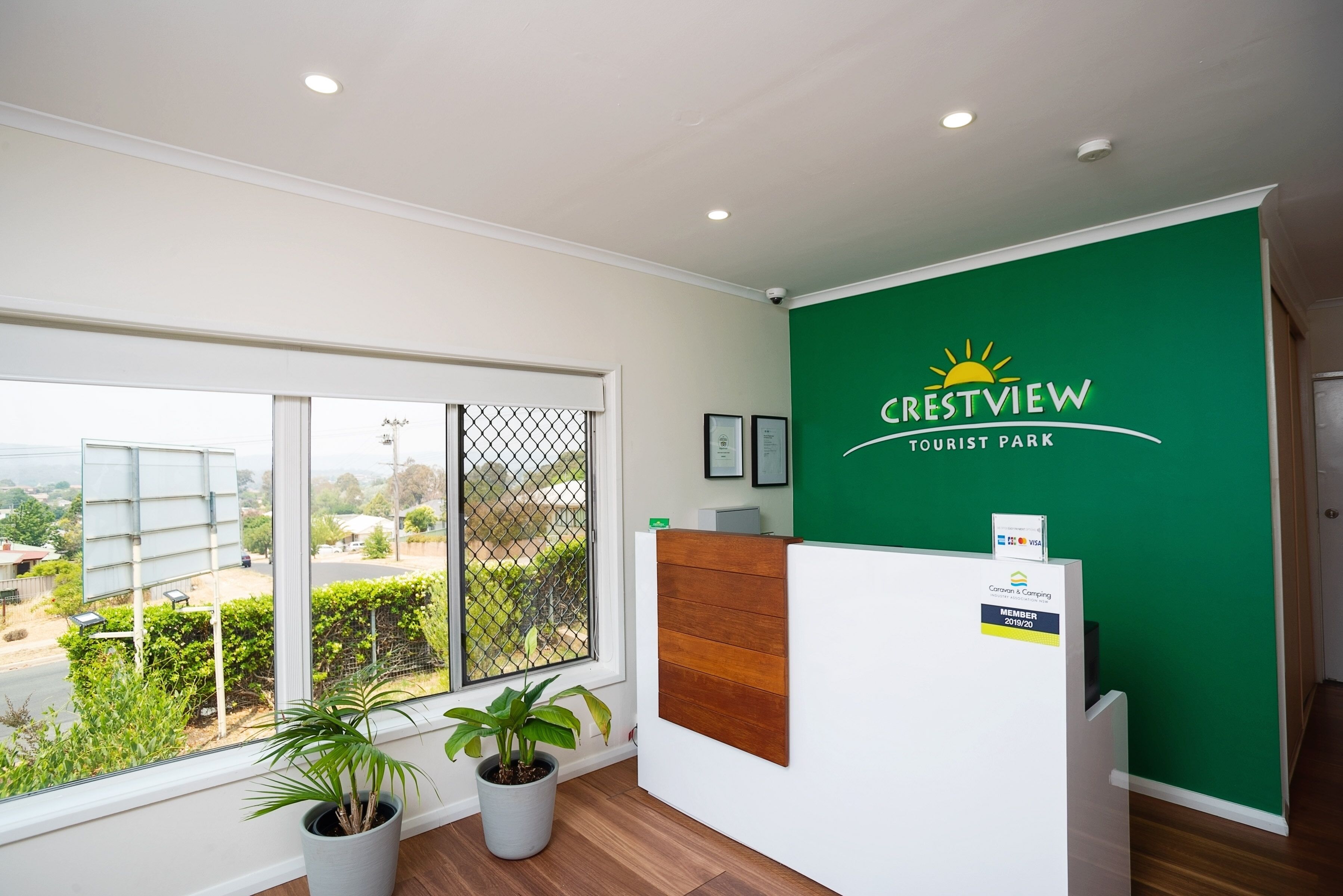 Un área de recepción con un amplio ventanal, una pared verde con el logotipo de Crestview Tourist Park y un panel de madera.