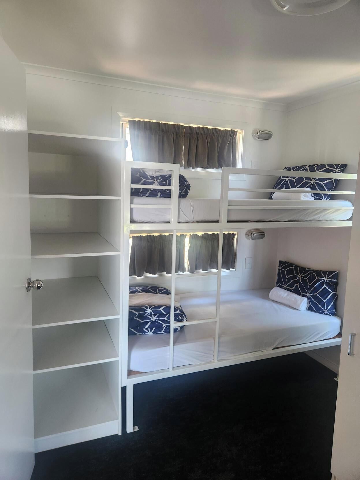 A bunk bed with a white frame, multiple shelves, and a door with a silver handle.