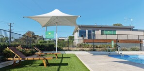 A pool area with lounge chairs and a canopy, a sign for Crestview Tourist Park, and a building with a sign. - Crestview Tourist Park (Karabar)
