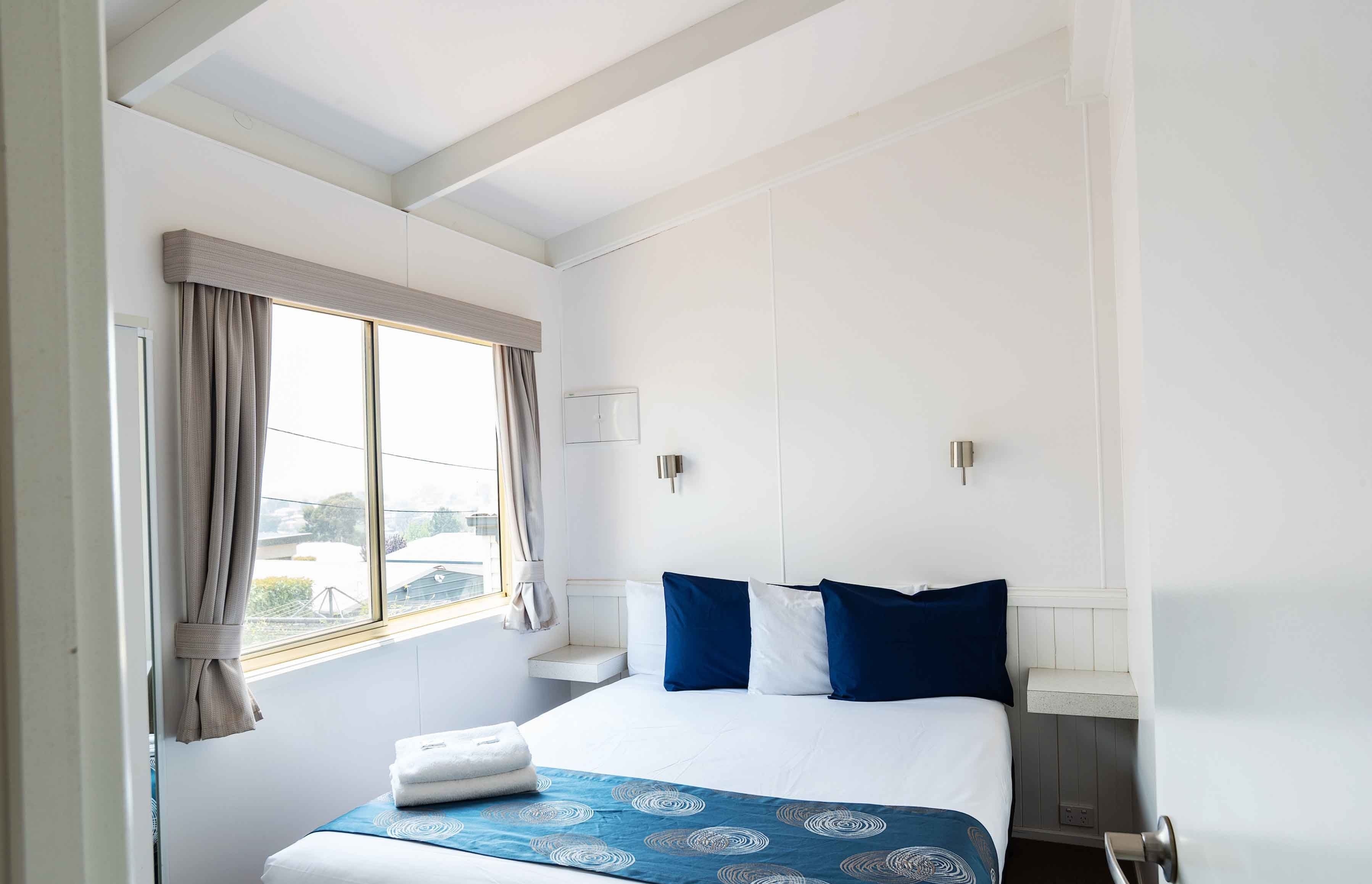A hotel room with a large bed, a window with curtains, a bedside table, and a wall-mounted light.
