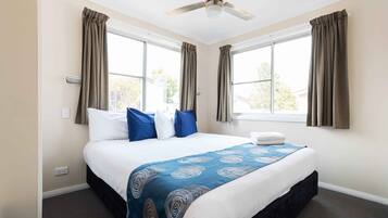 Una habitación de hotel con una cama, un ventilador de techo y dos ventanas con cortinas.