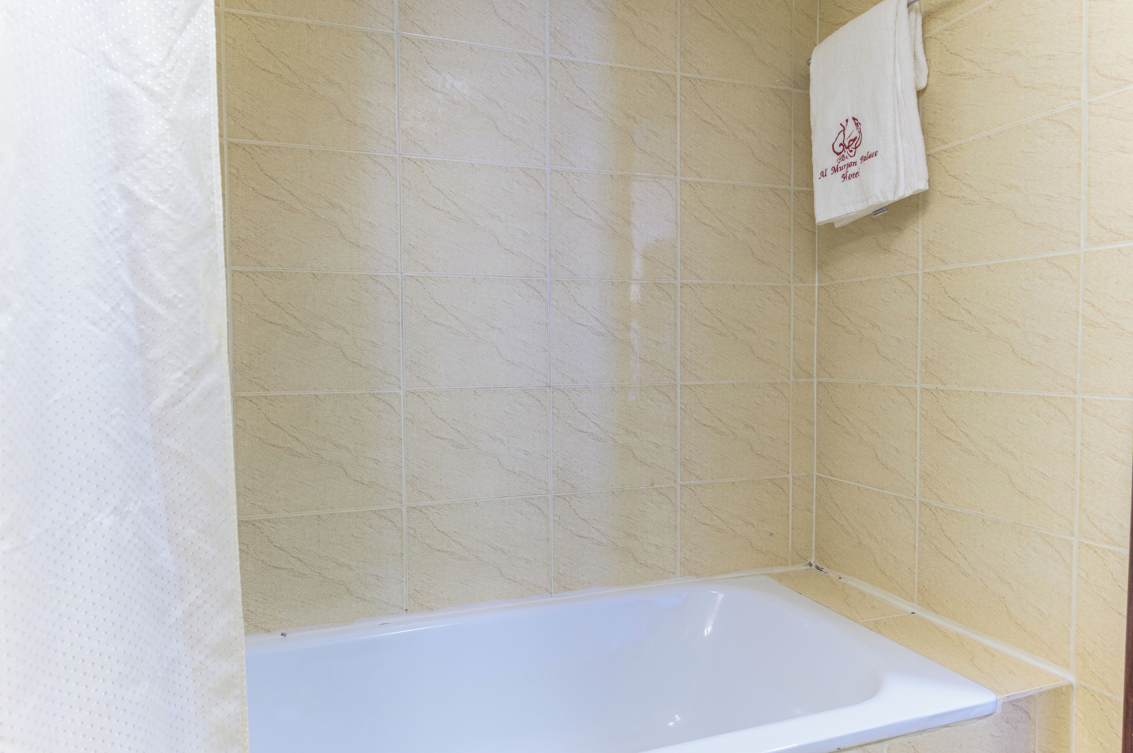 Un baño con bañera, paredes de azulejos color crema y una toalla blanca colgada en la pared.