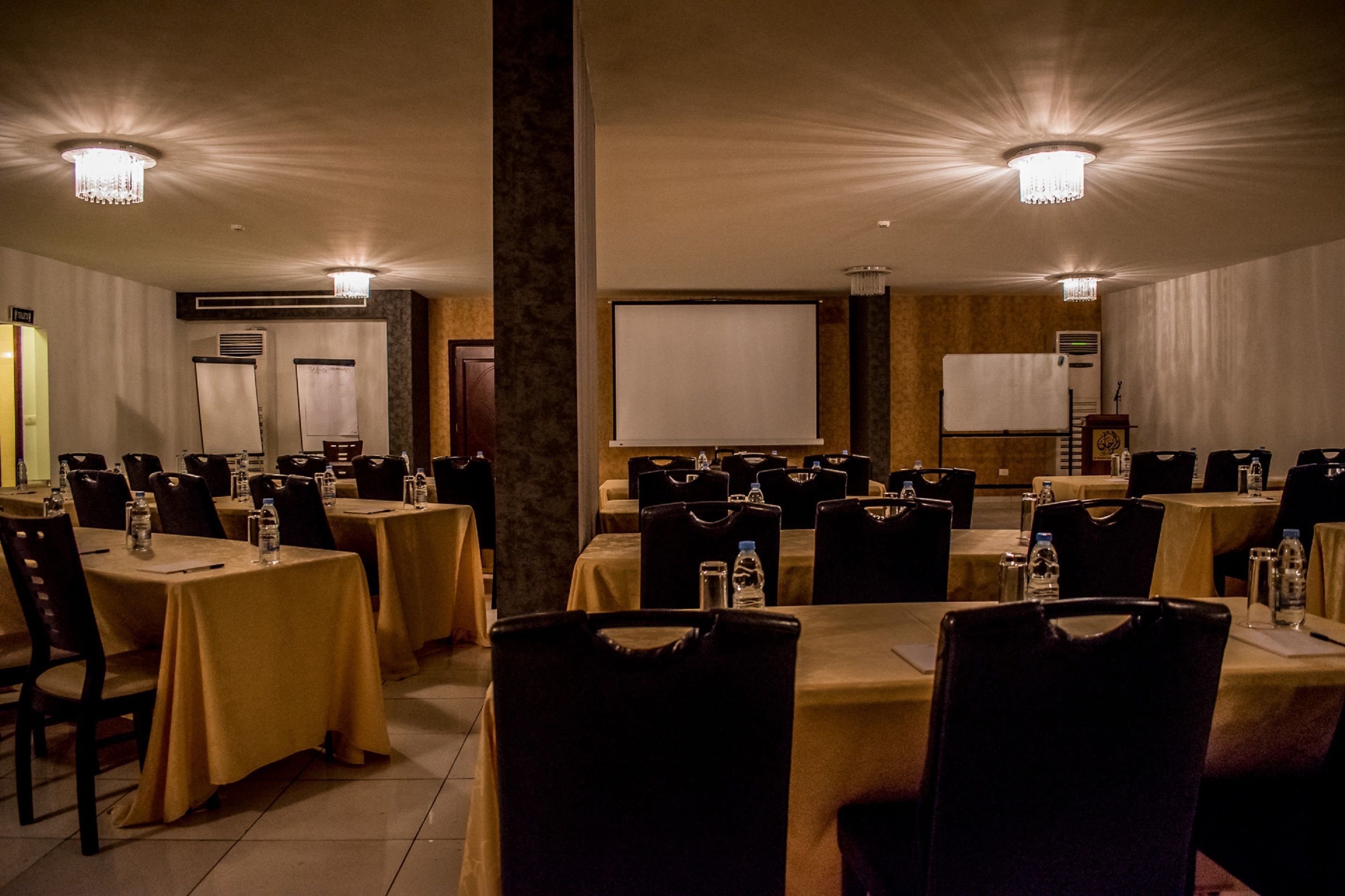 A conference room with multiple tables and chairs, equipped with water bottles and a projector screen.