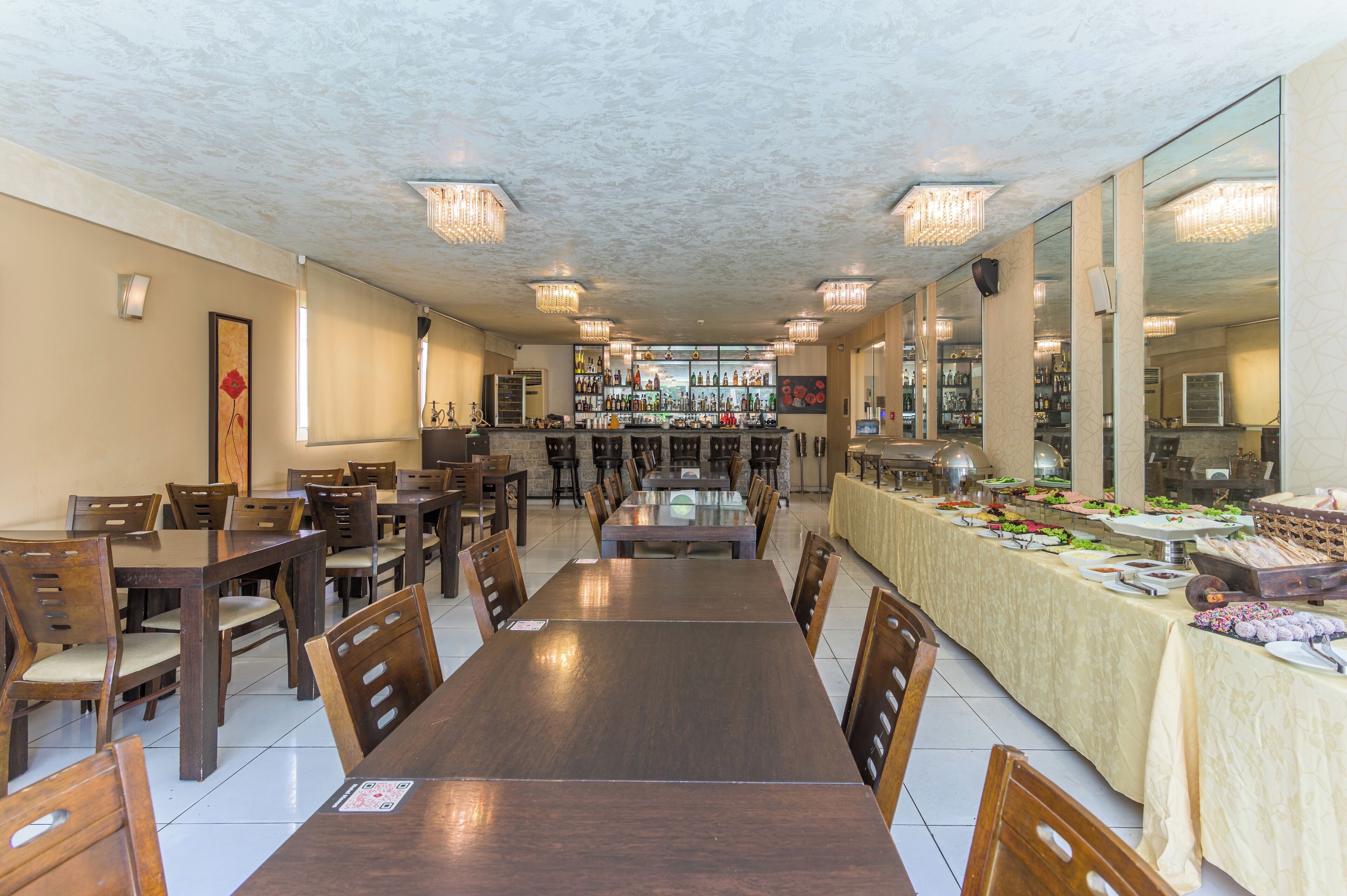 Un restaurante con varias mesas y sillas, una zona de bar con una variedad de botellas y un bufé con alimentos.