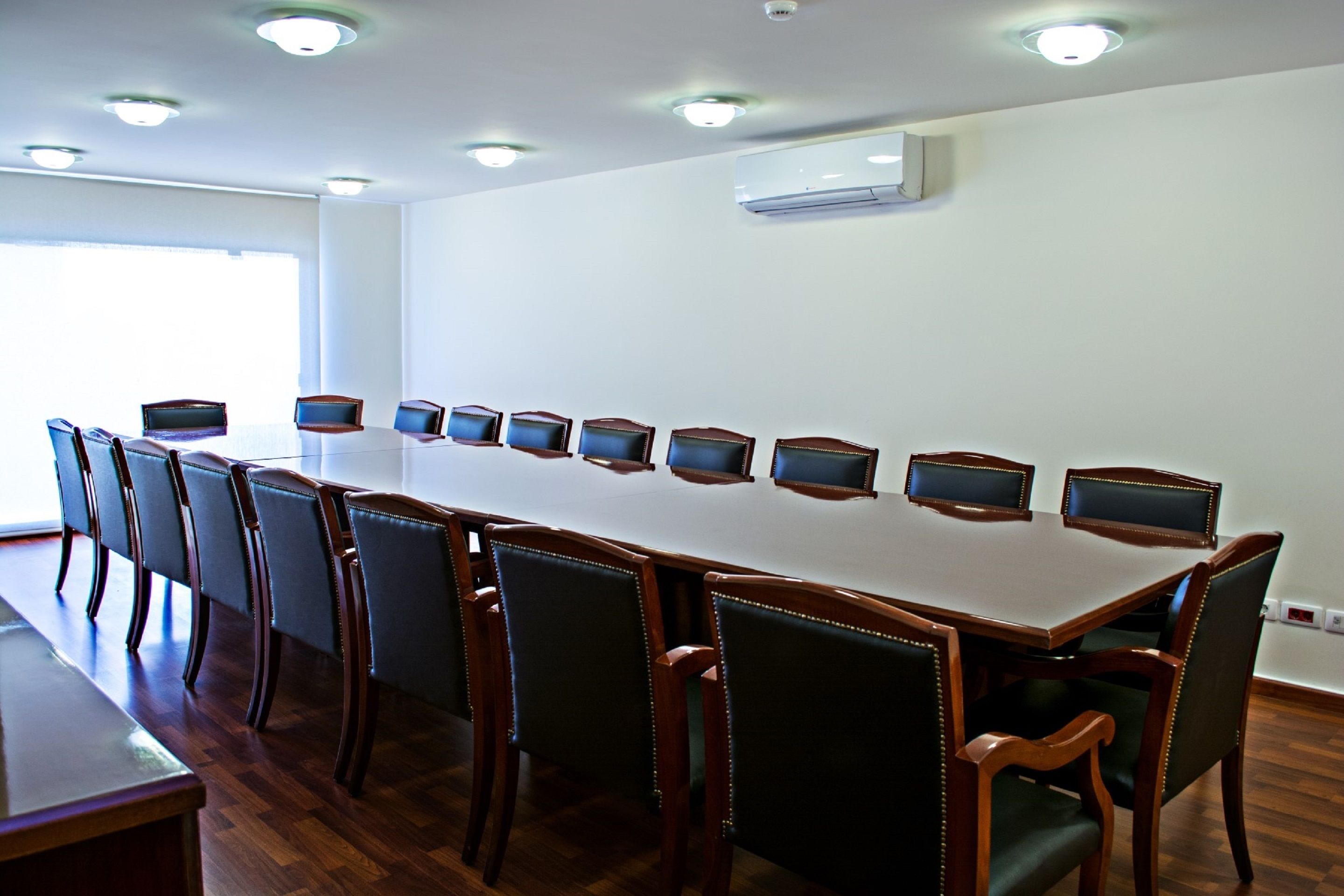 Un salón de conferencias con una mesa larga y 10 sillas, cada una con un ordenador portátil.