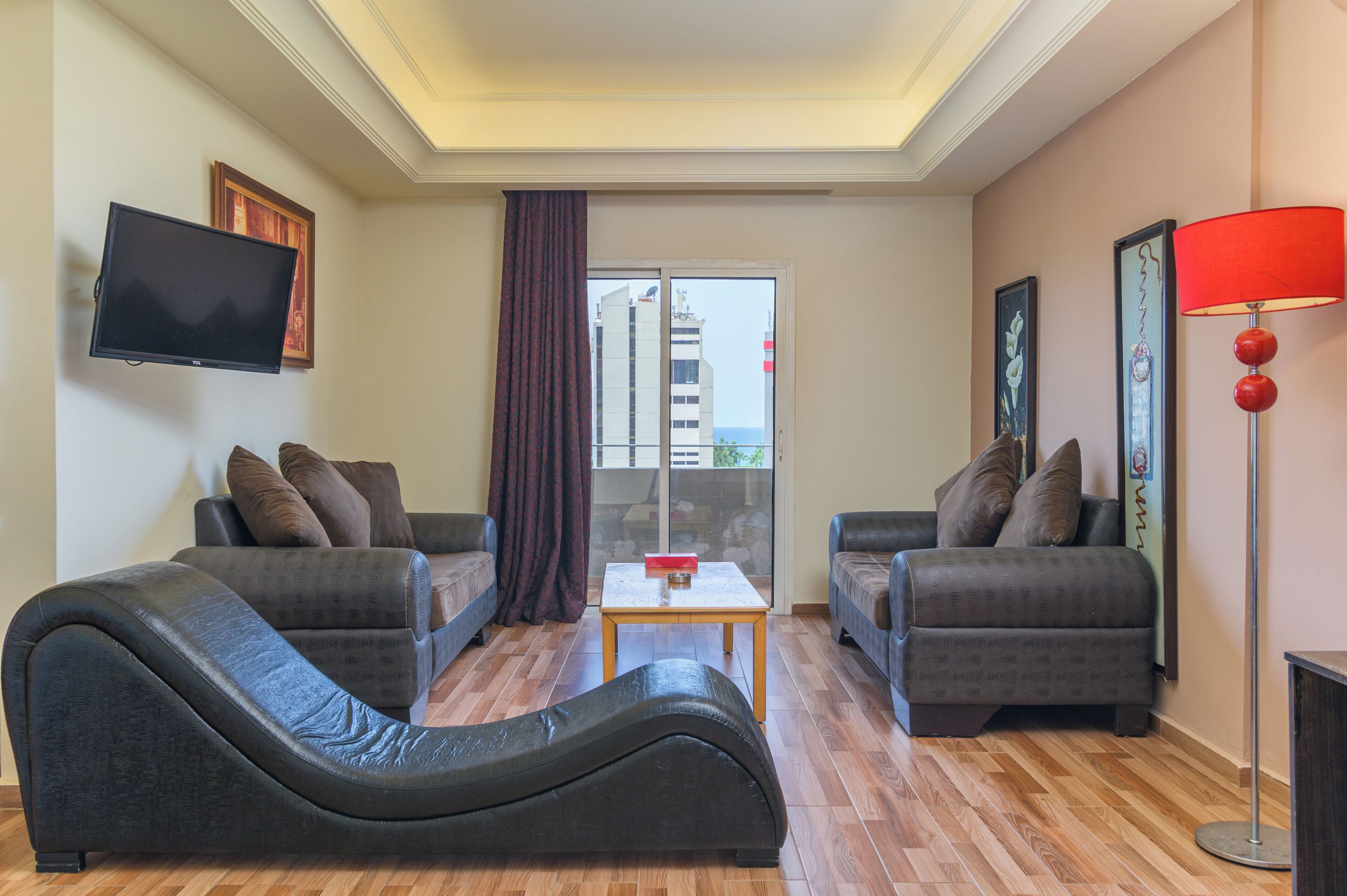 A modern living room with two sofas, a flat-screen TV, a red lamp, and a view through a glass door.