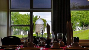 Un tavolo da pranzo apparecchiato con piatti, bicchieri e posate, con vista su un edificio e alberi attraverso una finestra.