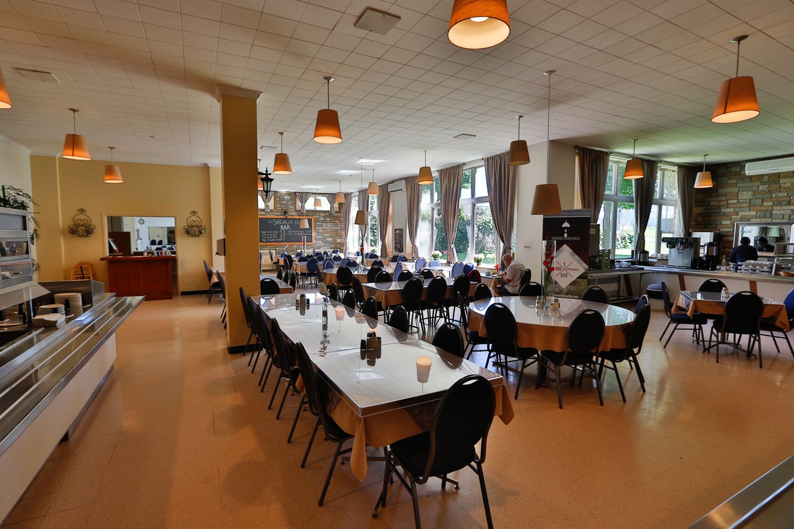 A spacious cafeteria with long tables and chairs, a buffet area, and large windows allowing natural light.
