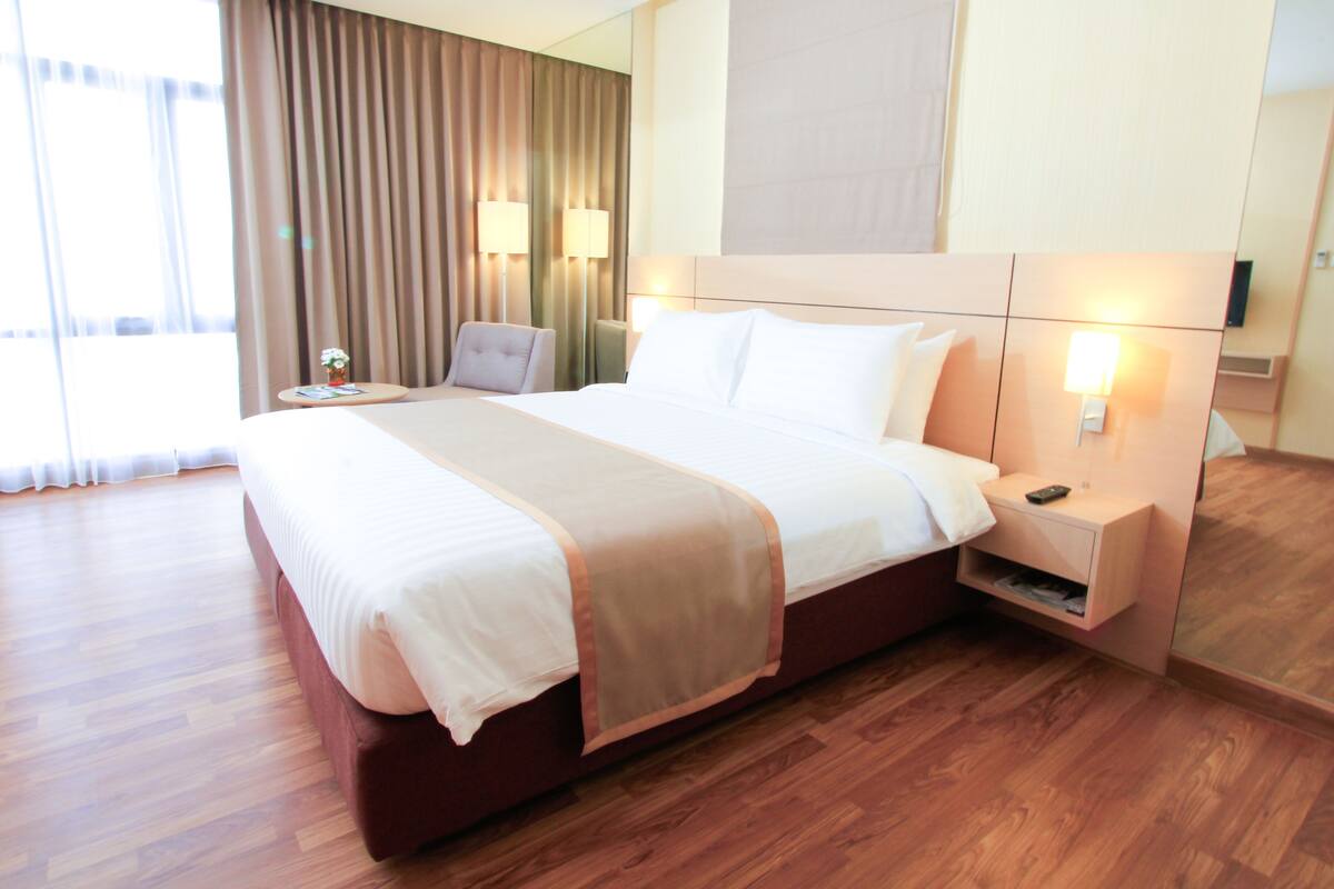A hotel room with a large bed, bedside lamps, a small table, and a chair.