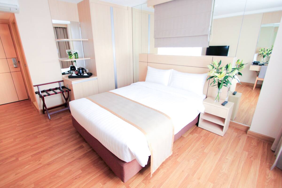 A modern hotel room with a large bed, a bedside table, a TV, and a mirror.