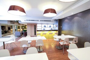 Un comedor moderno con mesas y sillas blancas, una zona de bar con taburetes e iluminación colgante.