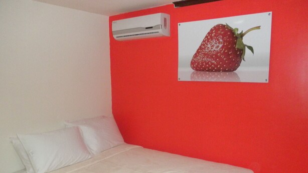 A bed with white linens and a white pillow, a red wall, and an air conditioning unit above the bed. - Pacific Dreams (Panama City)