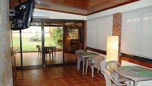 A patio area with a TV mounted on the wall, a table with chairs, and a brick wall. - Pacific Dreams (Panama City)