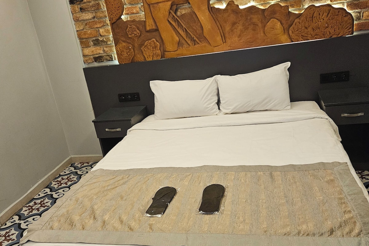 A hotel room with a brick wall, a bed with white bedding, and a patterned floor.