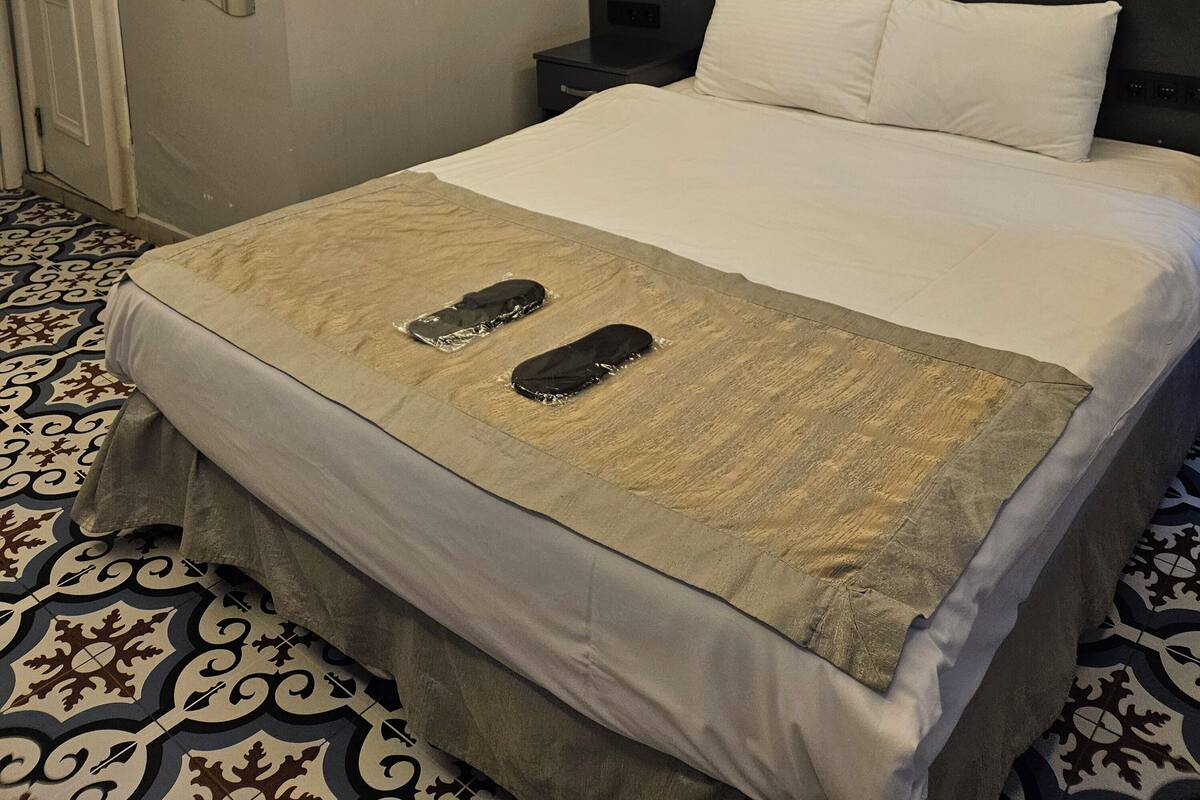 A hotel room with a bed, a brick wall mural, a patterned floor, and a door.