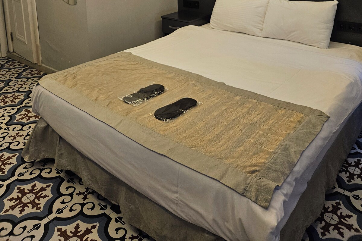 A hotel room with a bed, a brick wall mural, a patterned floor, and a door.