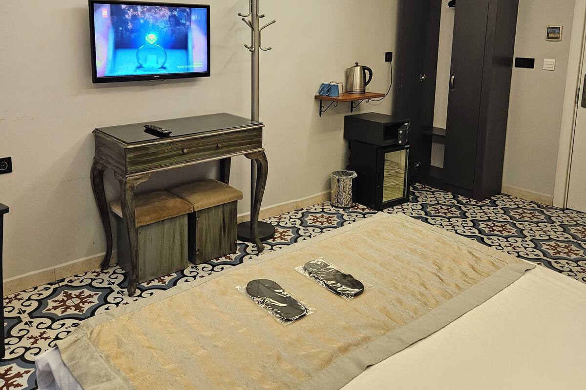 A hotel room with a bed, a television mounted on the wall, a small desk, a coat rack, and a wardrobe.