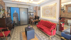 A room with a red sofa, a wooden piano, a patterned carpet, and a large decorative mirror. - A Plus Residence (Istanbul)
