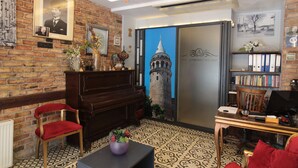 A room with a brick wall, a piano, a red chair, a table with a vase, and a bookshelf with binders. - A Plus Residence (Istanbul)