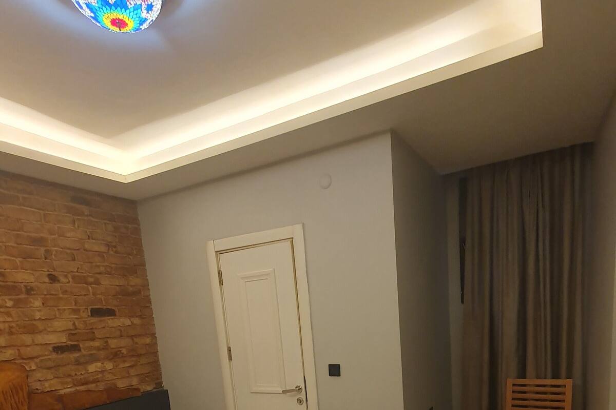 A hotel room with a large bed, a wooden headboard, a small bedside table, a desk, a chair, a suitcase, and a door.