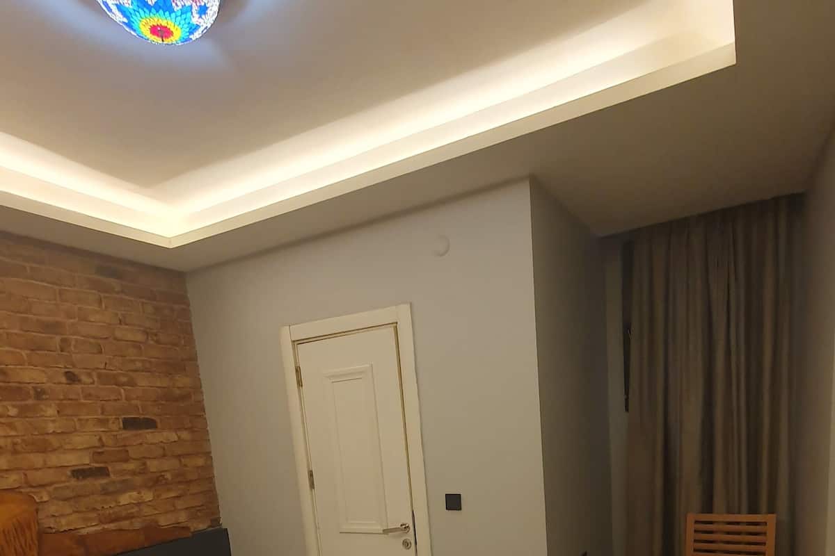 A hotel room with a large bed, a wooden headboard, a small bedside table, a desk, a chair, a suitcase, and a door.