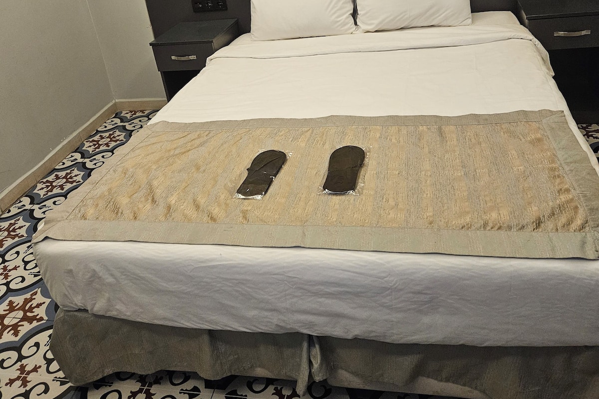 A hotel room with a brick wall, a bed with white bedding, and a patterned floor.
