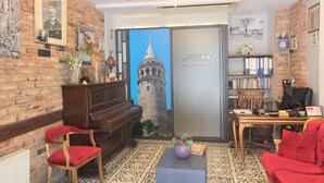 A room with a piano, a red chair, a bookshelf, and a large window with a view of a tower. - A Plus Residence (Istanbul)