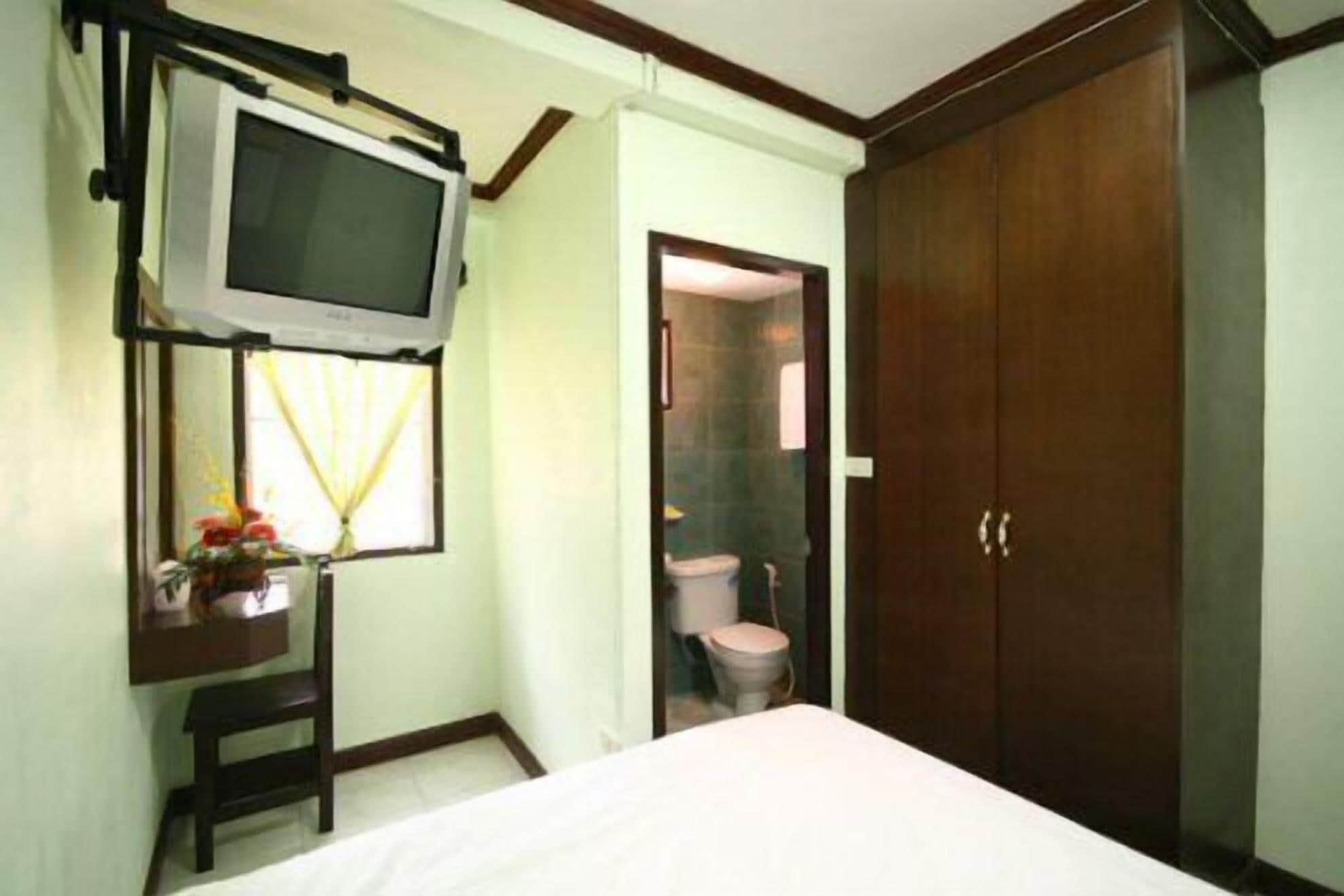 Une chambre à coucher avec un lit, un téléviseur fixé au mur, une armoire en bois et une salle de bain visible à travers une porte ouverte.