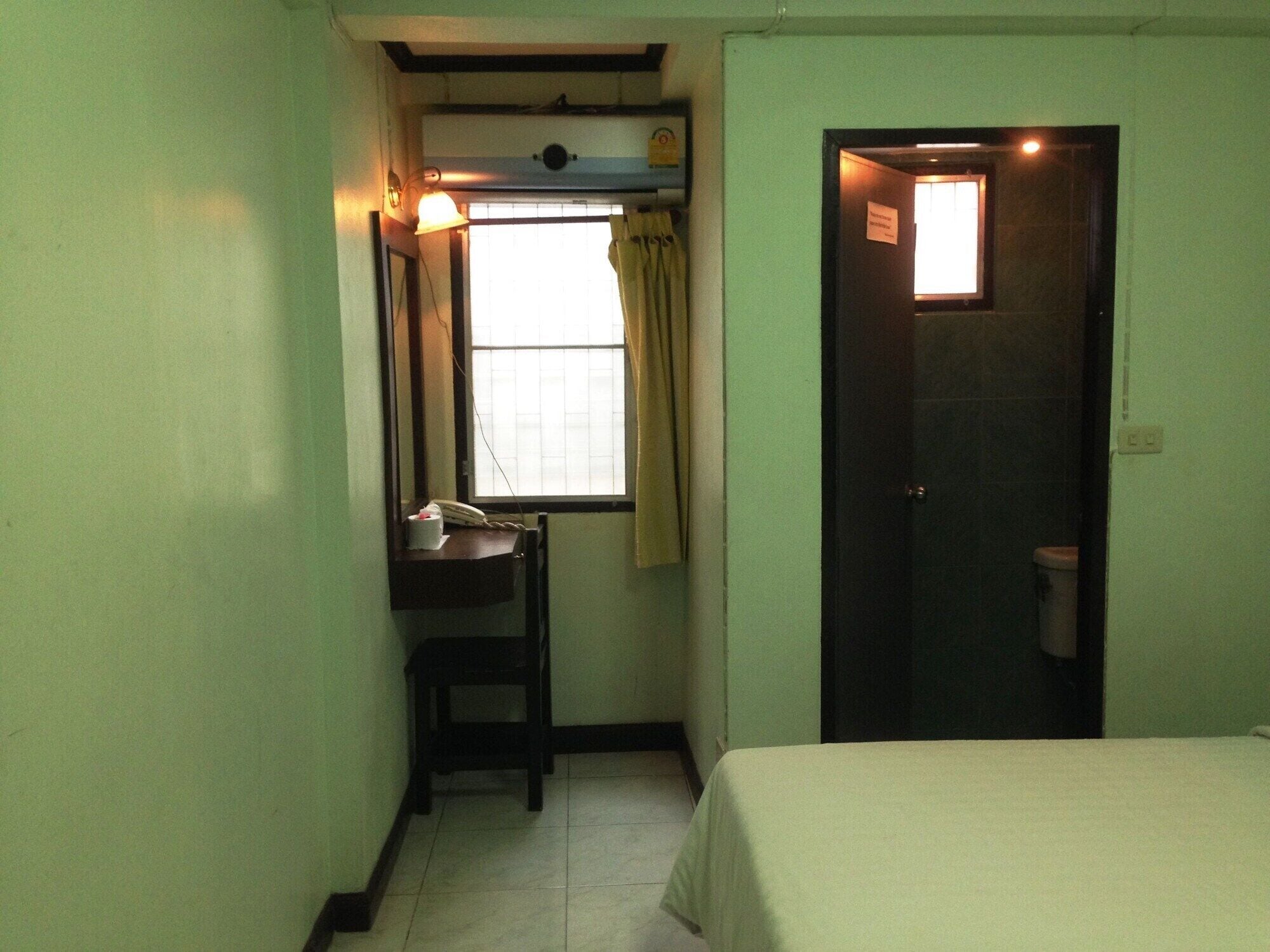 A small, narrow room with a bed, a desk with a telephone, and a window with curtains.
