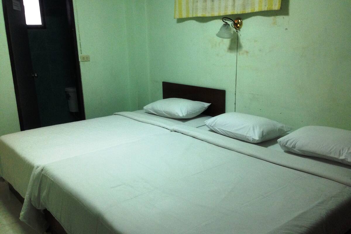Quarto com uma cama de solteiro, travesseiros brancos e cabeceira simples.