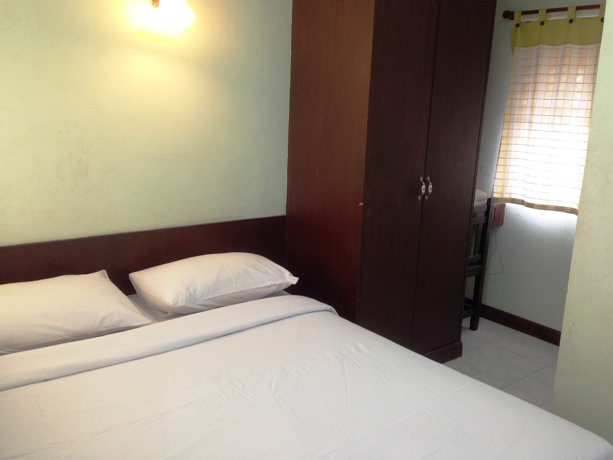 A bedroom with a bed, two pillows, a wooden wardrobe, and a window with a curtain.
