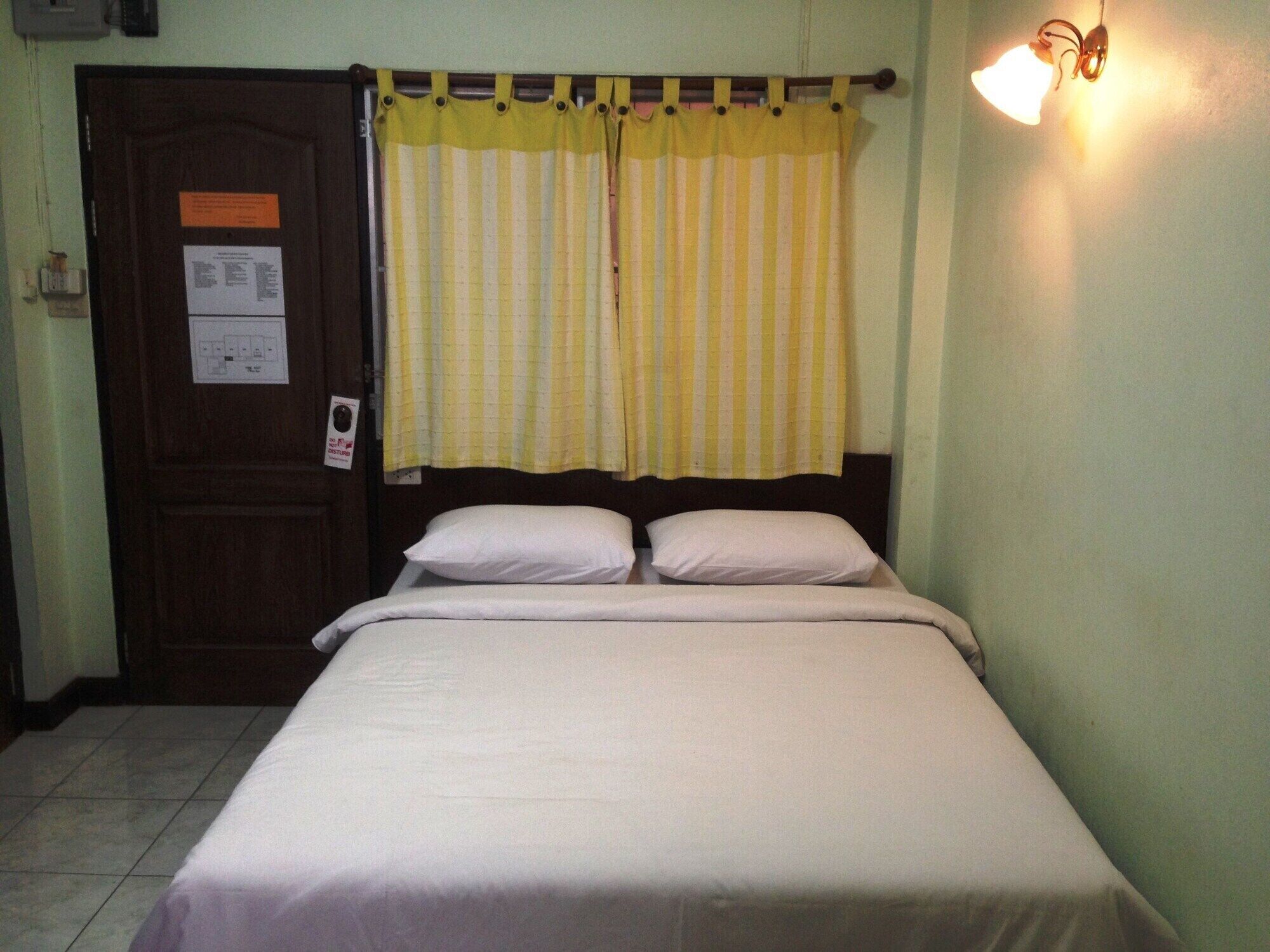 A single bed with white bedding in a room with a wooden door and a yellow-striped curtain.