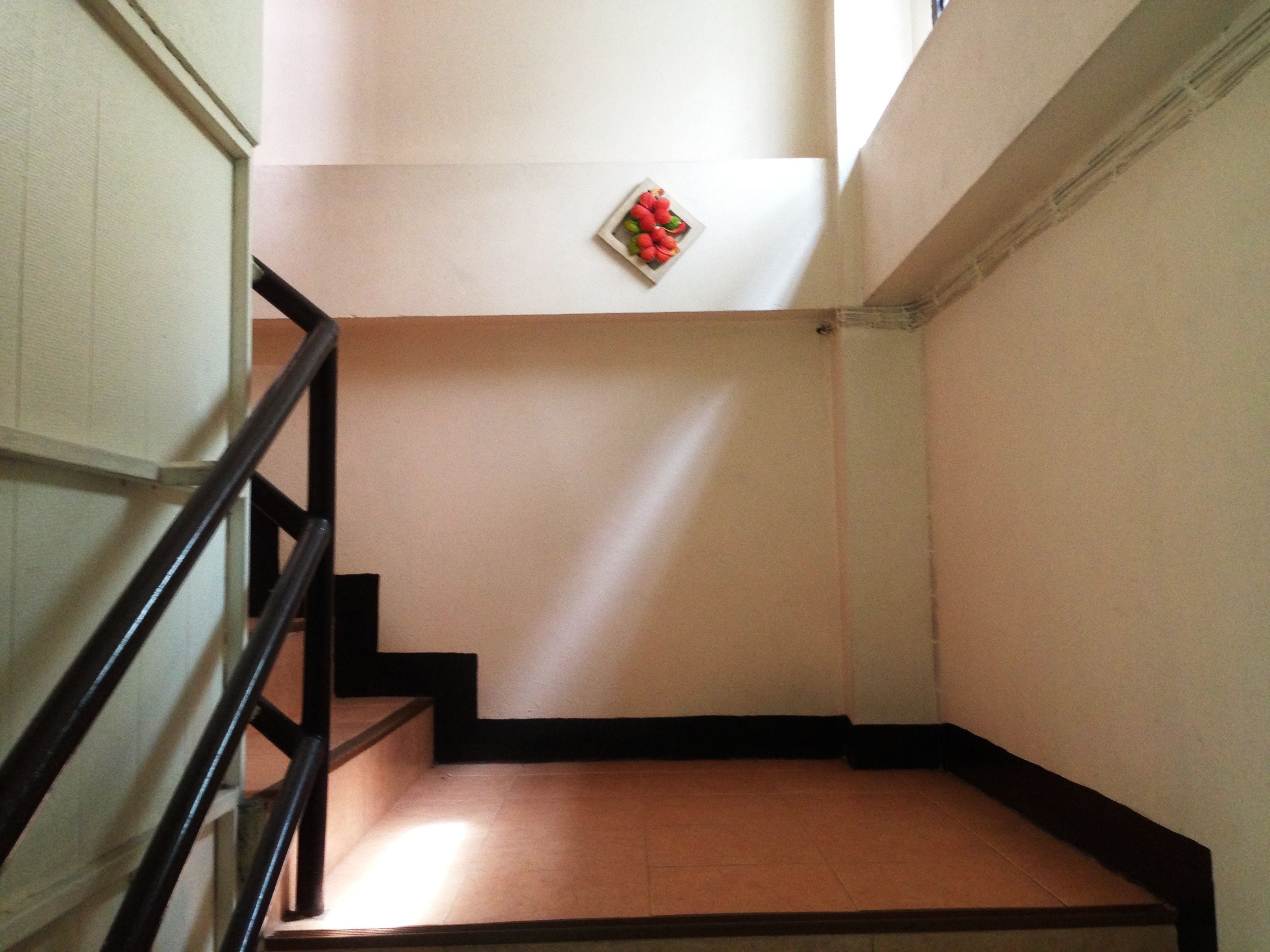 A staircase with a handrail, a small plate with fruit on the wall, and a tiled floor.