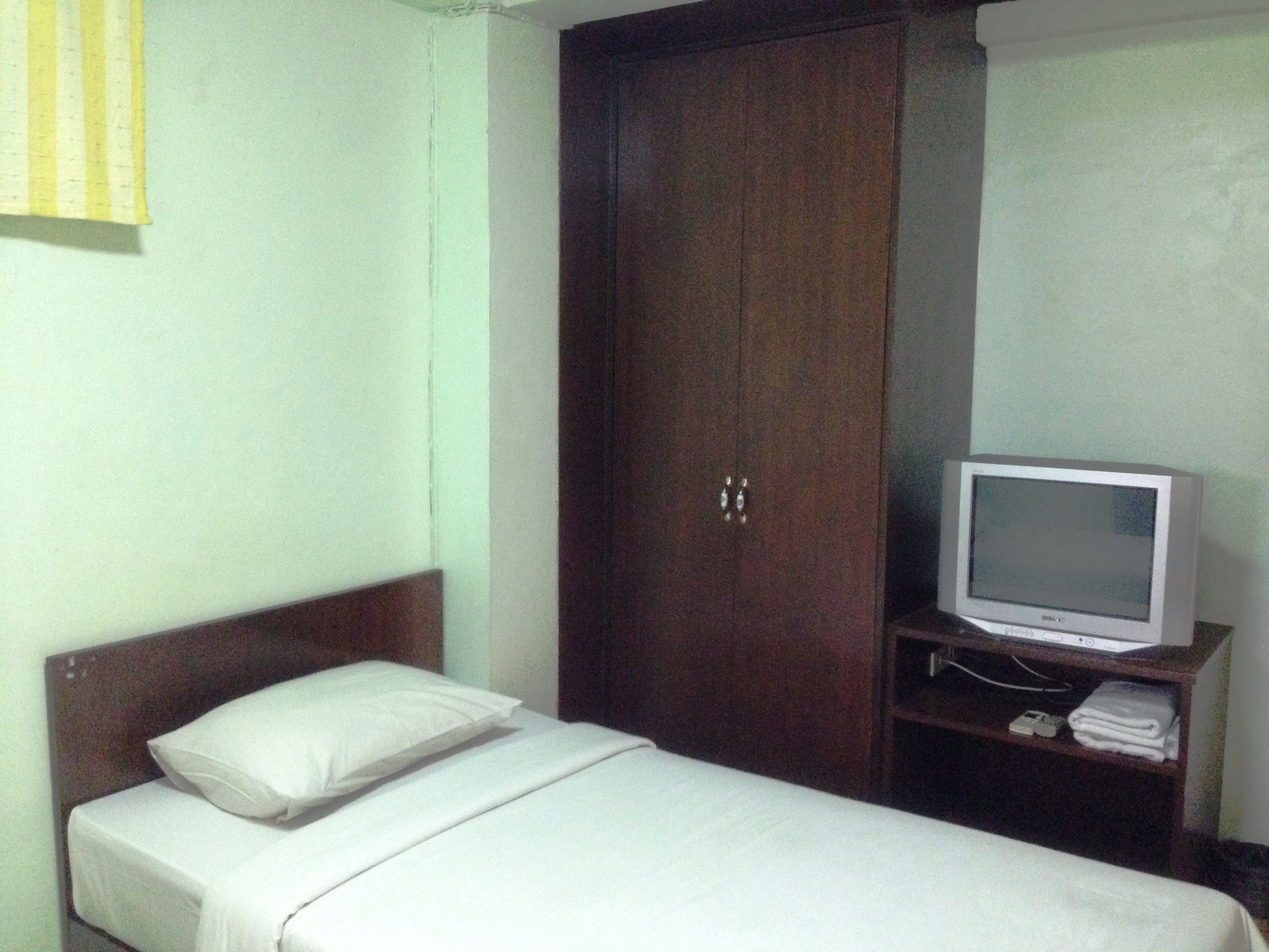 A single bed with white bedding, a wooden wardrobe, and a television on a wooden stand.