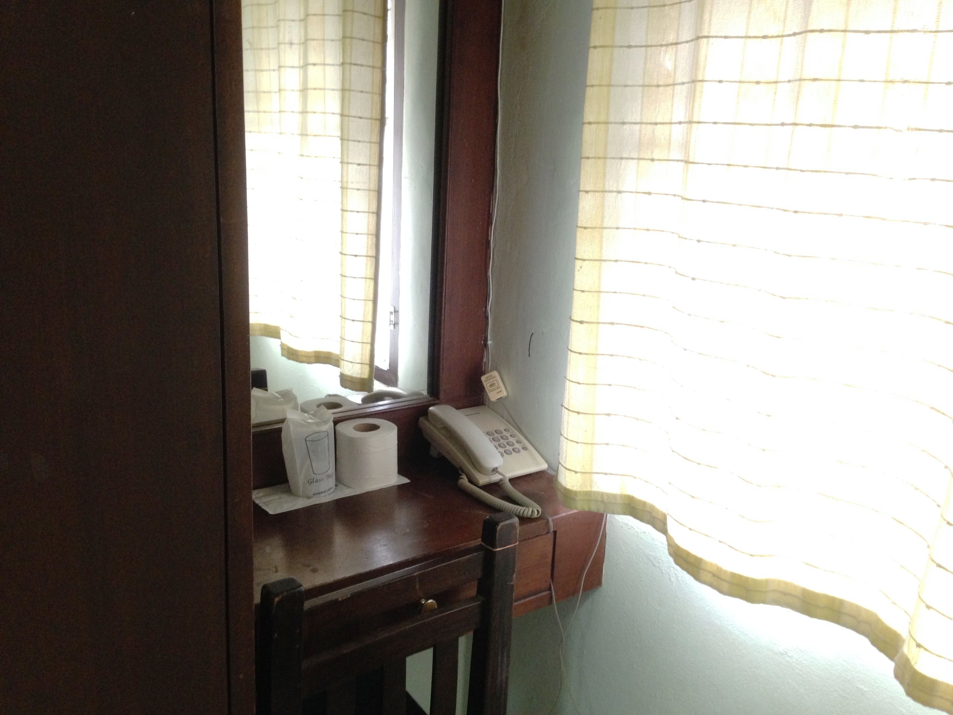 A wooden desk with a telephone, a glass of water, and a roll of toilet paper.