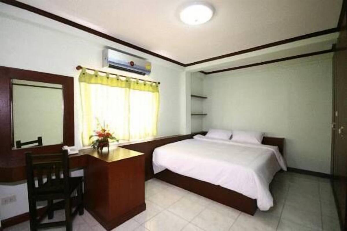 Quarto de hotel com cama, escrivaninha, cadeira, espelho, janela com cortinas e ventilador de teto.
