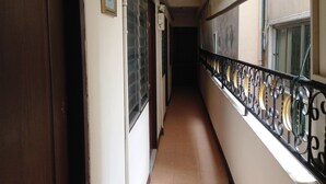 A corridor with a tiled floor, a wooden door on the left, and a balcony with a metal railing on the right.
