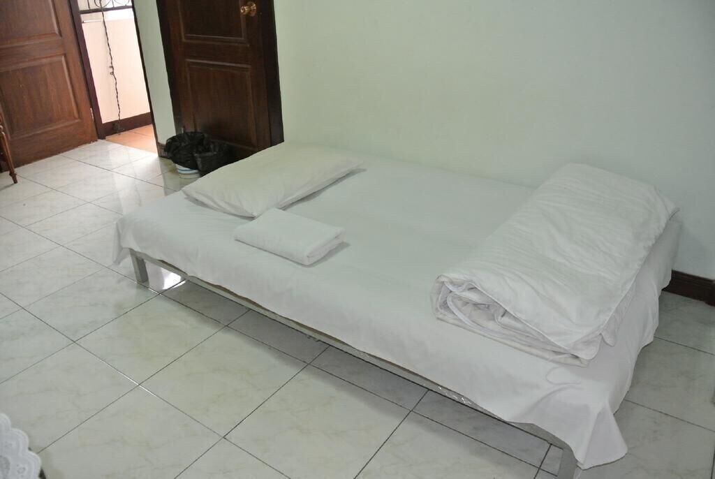 Een enkel bed met witte lakens in een kamer met betegelde vloer en een houten deur.