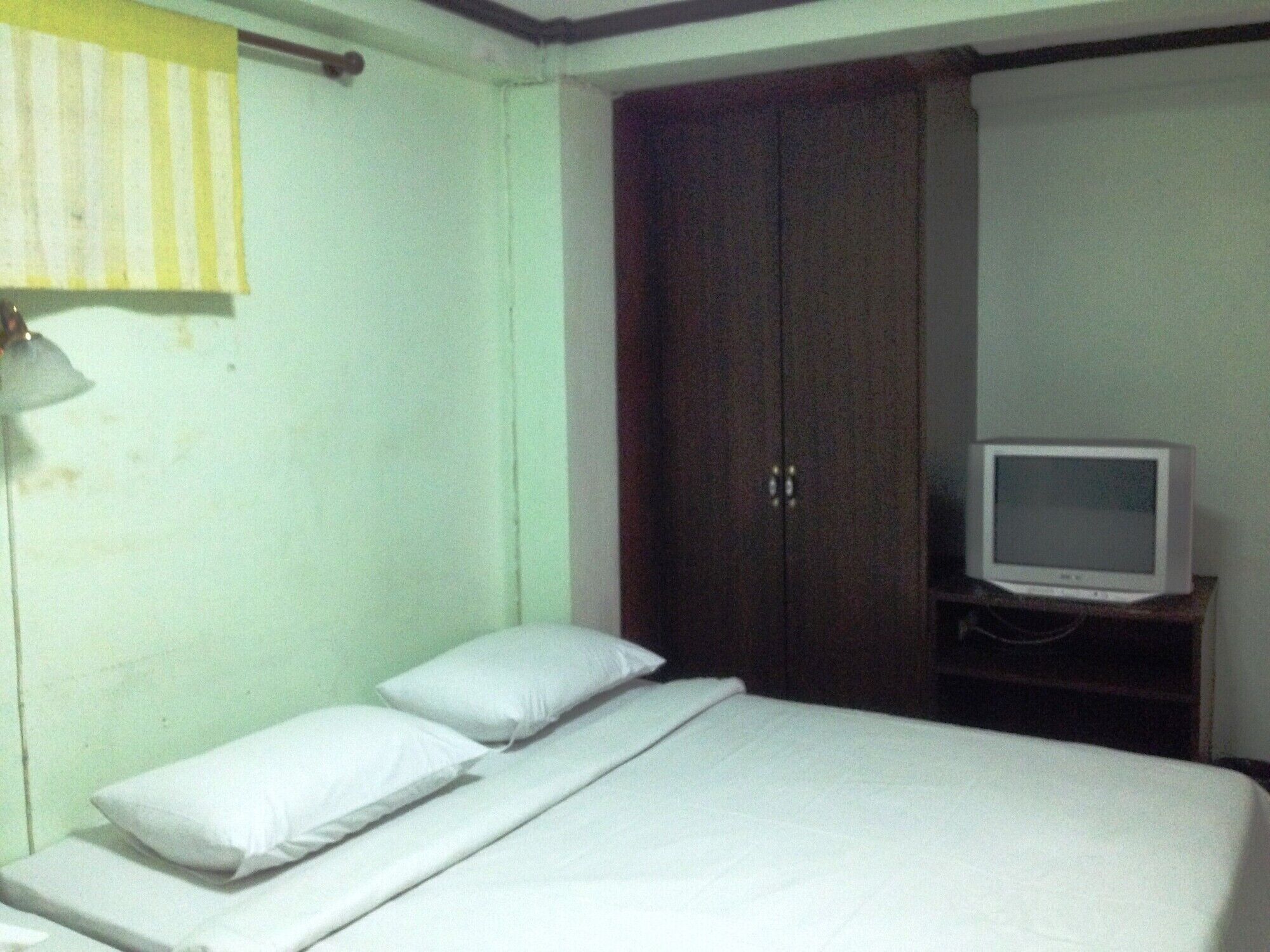Ein schlichtes Zimmer mit Bett, Kissen, Schrank und Fernseher.