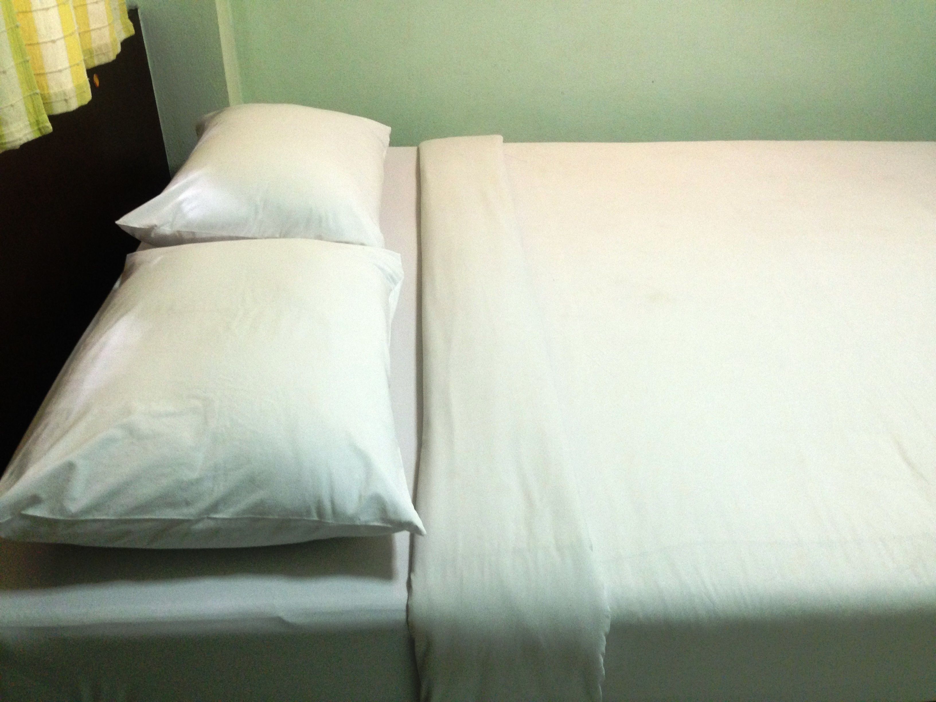 A bed with white bedding and pillows in a room with a green wall.